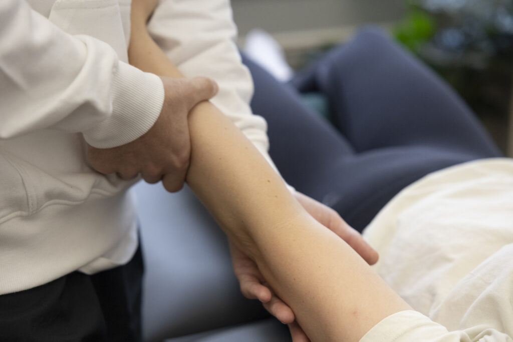 Eine Person in einem weißen Hemd hält und untersucht sanft den ausgestreckten Arm einer anderen Person, während einer Physio Lübeck oder einer medizinischen Untersuchung.